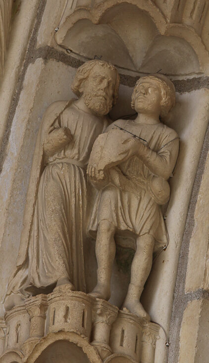 Statues carved into a Cathedral wall featuring a bearded Mordecai talking to a beardless eunuch who holds a scroll