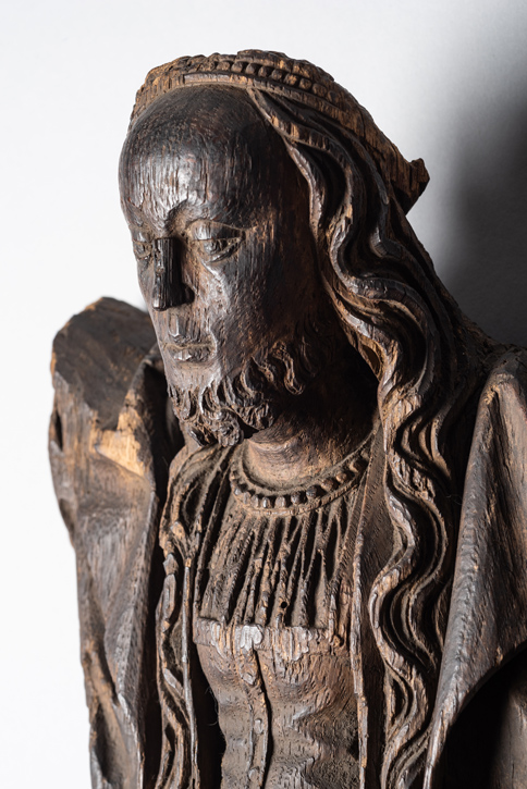 Closeup of part of a wooden statue, a figure with long hair, a beard, and feminine dress